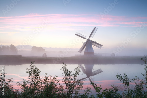 windmill by river at misty sunrise