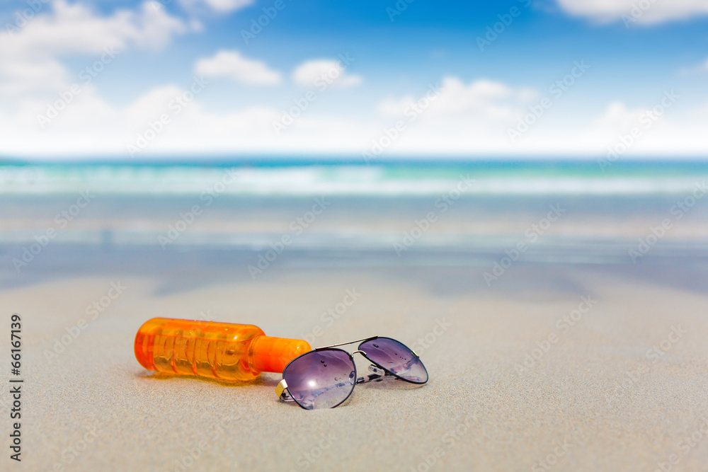 Sunscreen lotion and dark glasses on the beach for summer time Sunscreen lotion and dark glasses on the beach for summer time