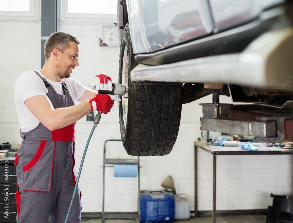Cheerful serviceman unscrewing wheel in car workshop Cheerful serviceman unscrewing wheel in car workshop