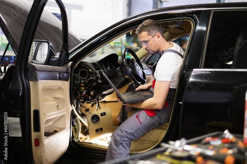 Serviceman making car diagnostics with laptop in a workshop photo