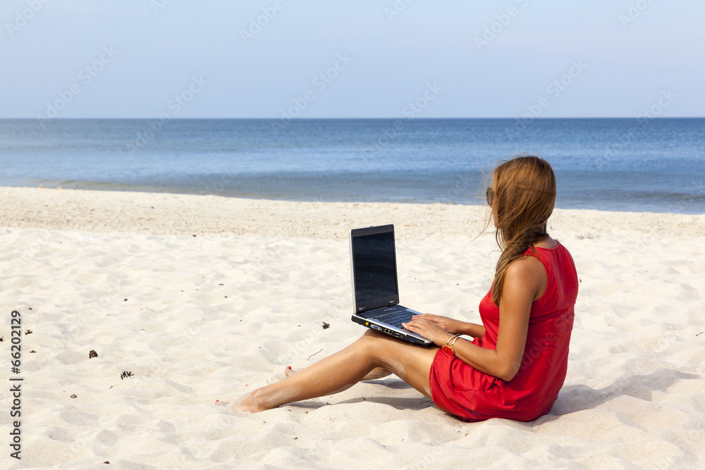 Woman is sitting with laptop on the beach.