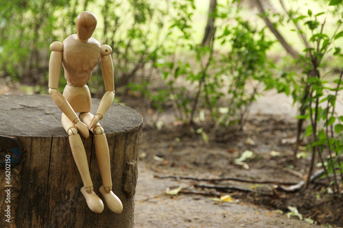 Wooden pose puppet sitting on wooden timber, outdoors