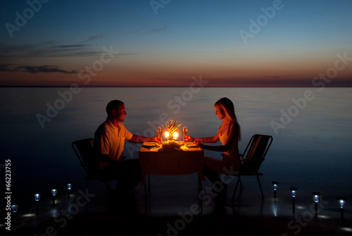 Obraz na plátně A young couple share a romantic dinner with candles on the beach
