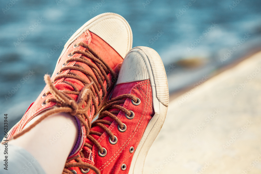 red trendy sneakers on girl and seascape as background