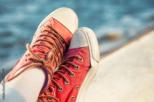 red trendy sneakers on girl and seascape as background