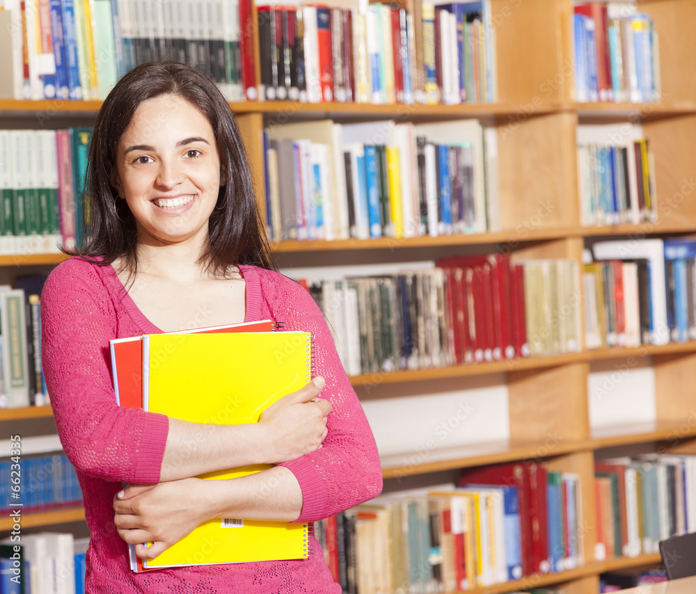 Happy female student holding books at the library Happy female student holding books at the library