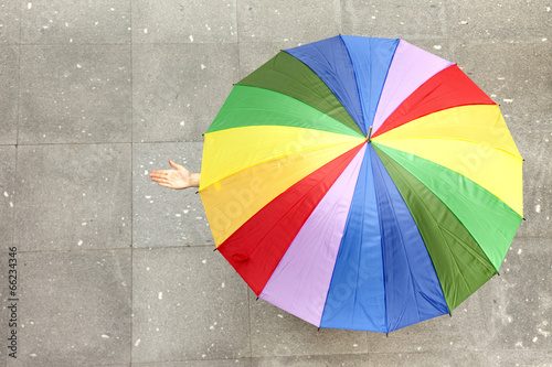 Woman hidden under multicolored umbrella and checking if it's ra