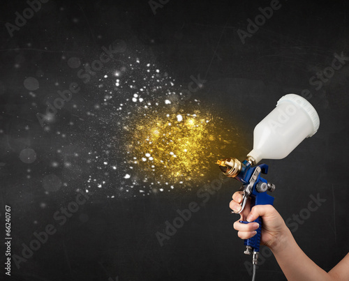 Worker with airbrush painting with glowing golden paint