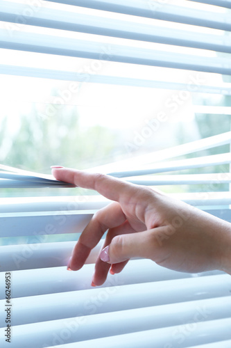 Female hand separating slats of venetian blinds with a finger