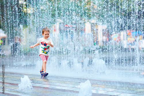 excited boy running between water flow in city park