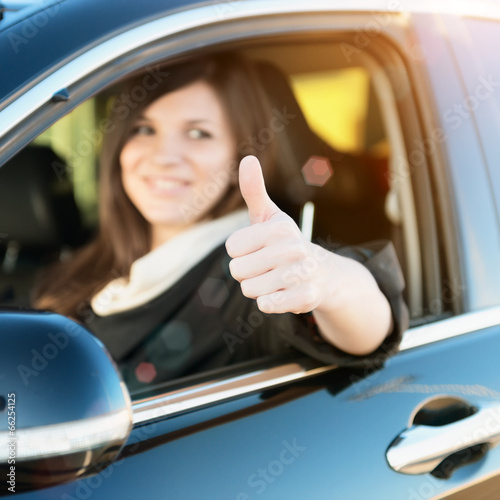 Pretty young woman with thumbs up in her new car