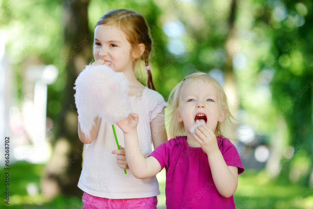 Obraz premium Adorable little sisters eating candy-floss
