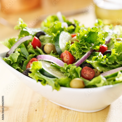 bowl of leafy green salad with olives, tomatoes and cucumber.