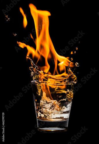 Glass with whiskey splash and fire on black background
