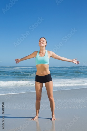 Fit woman standing on the beach with arms out