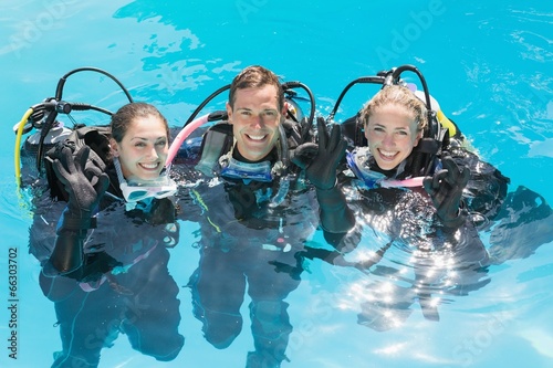 Smiling friends on scuba training in swimming pool looking at ca