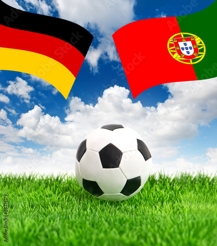 soccer ball on green grass and flags of germany and portugal