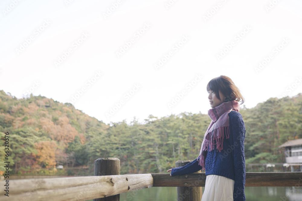 Fototapeta premium 秋の紅葉の公園の池のほとりで池を見つめる女性