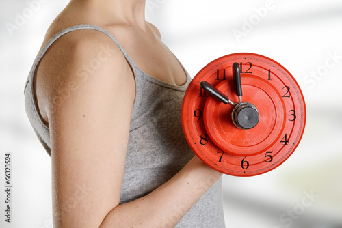 Beginner female athlete holding dumbbell with clock dial. Time f