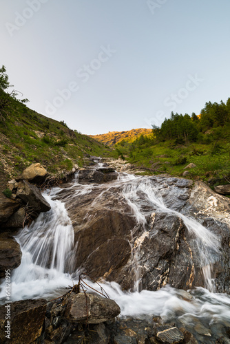 Mountain stream flowing on very steep eroded rocky slopes at sun