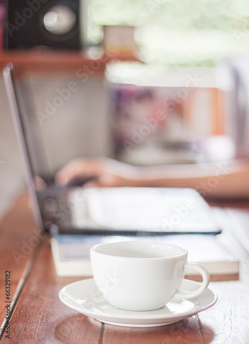 Woman using laptop with a white cup of coffee