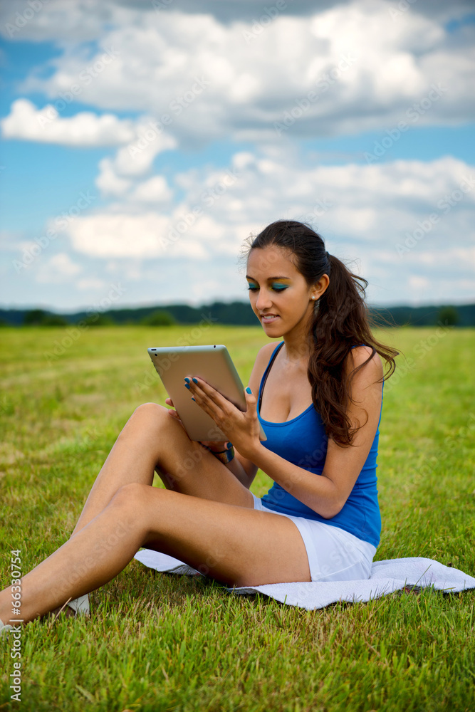 Beautiful woman using a tablet sitting on meadow Beautiful woman using a tablet sitting on meadow