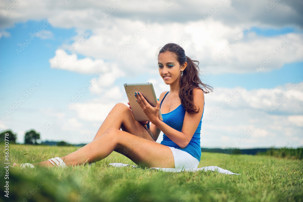 Beautiful woman using a tablet sitting on meadow Beautiful woman using a tablet sitting on meadow