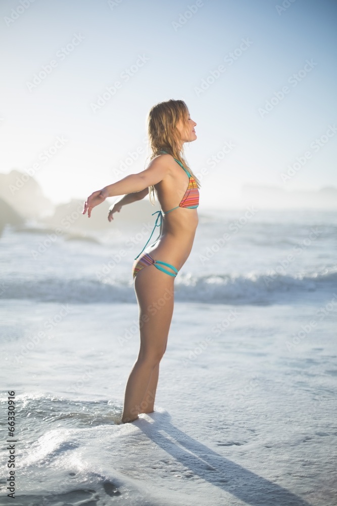 Content blonde standing on the beach in bikini with arms out