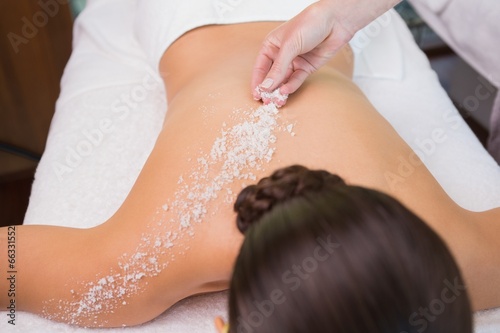 Beauty therapist pouring salt scrub on womans back