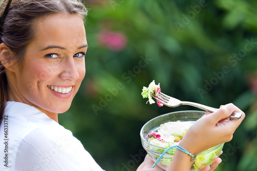 Beautiful young woman holding green salad, outdoors