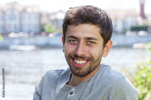 Laughing man with beard in a grey shirt on a river