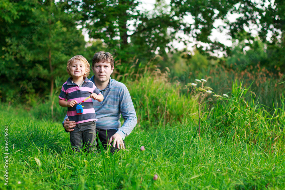 Little boy and his father sitting on grass in summer forest Little boy and his father sitting on grass in summer forest
