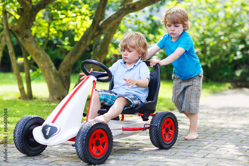 Two happy twin boys driving toy car