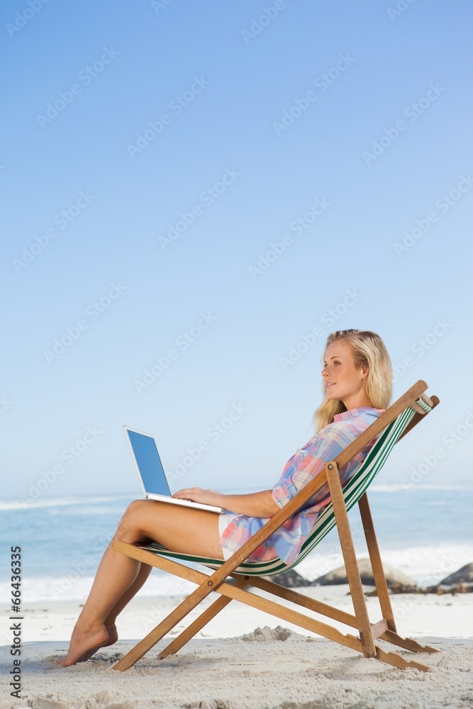 Pretty blonde sitting on beach using her laptop