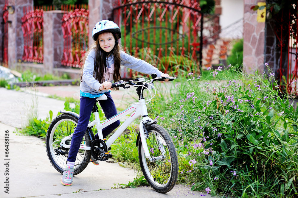 Fototapeta premium Adorable kid girl in blue helmet riding her bike 