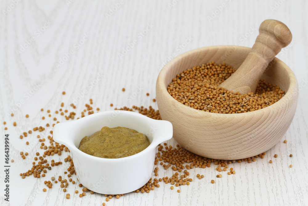 Mustard seeds in wooden mortar and mustard in white bowl Mustard seeds in wooden mortar and mustard in white bowl