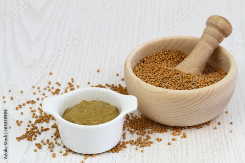 Mustard seeds in wooden mortar and mustard in white bowl