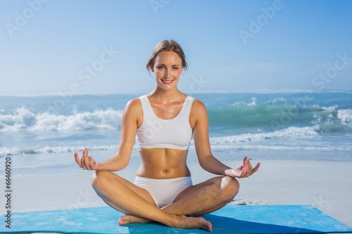 Fit smiling woman sitting in lotus pose on the beach