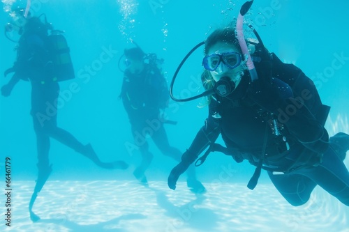 Friends on scuba training submerged in swimming pool one looking