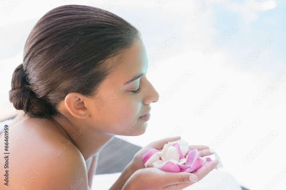 Smiling brunette lying on towel holding rose petals Smiling brunette lying on towel holding rose petals