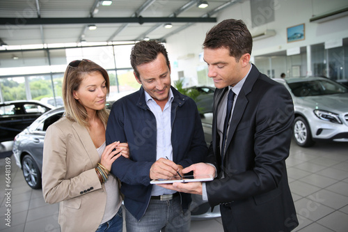 Couple signing car purchase order on digital tablet