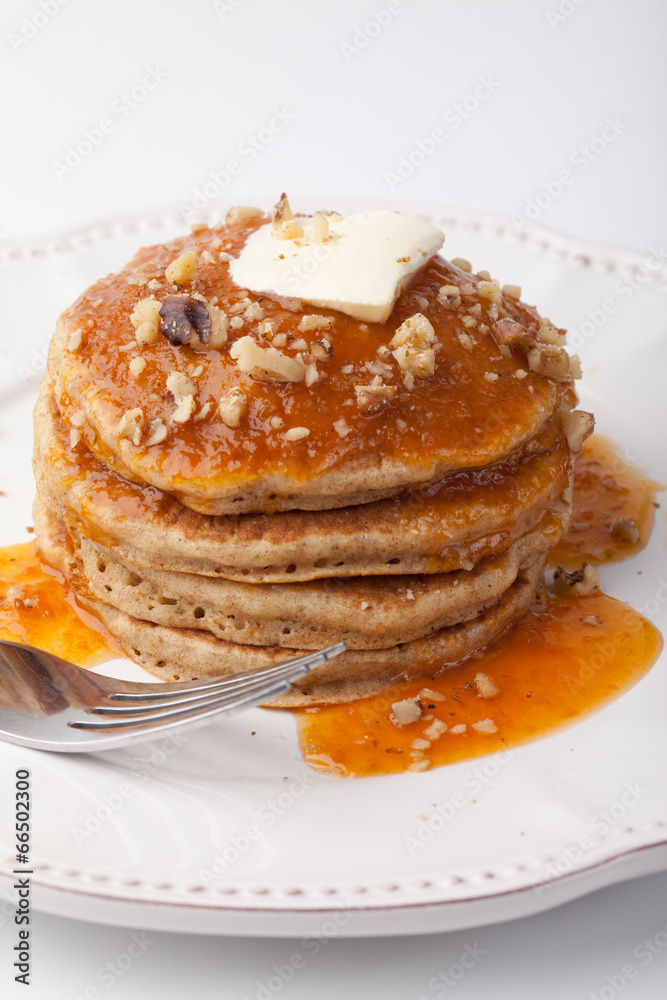 Wholesome homemade whole wheat pancakes with an apricot sauce topped with butter and chopped walnuts on a white background