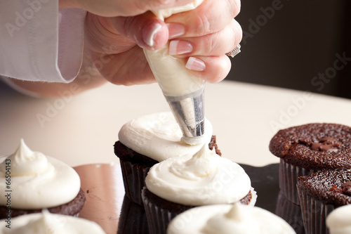Valokuva Chef decorating and piping buttercream icing on chocolate filled chocolate cupca