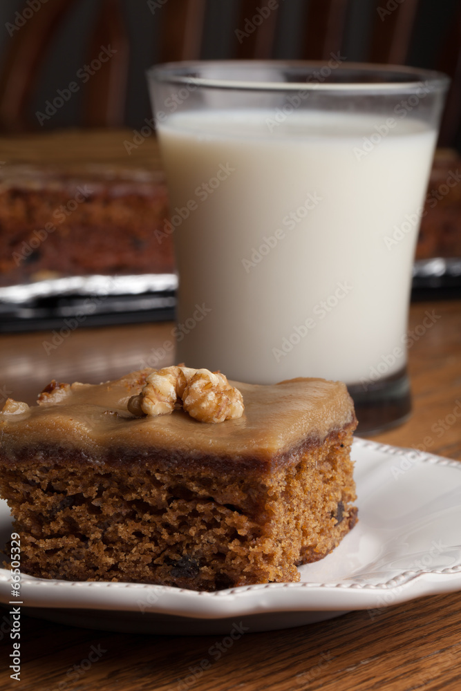 Macro shot of carrot cake topped with a walnut next to a glass of cold milk with whole cake in background Macro shot of carrot cake topped with a walnut next to a glass of cold milk with whole cake in background