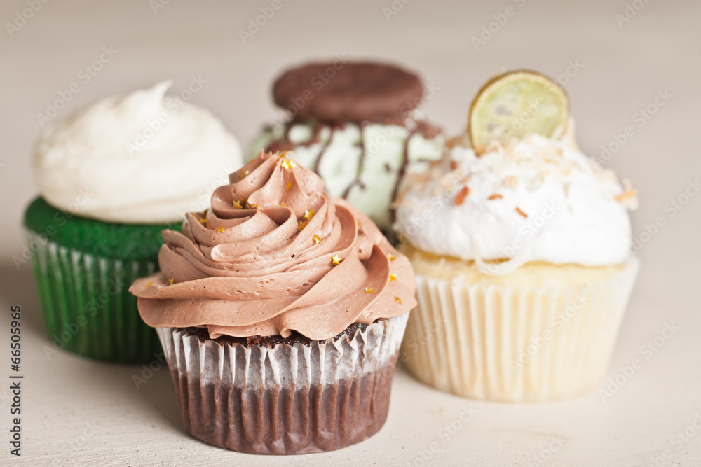 Coconut Key Lime Cupcake, Pot of Gold Chocolate Caramel Cupcake, Irish Mint Chocolate Cupcake, and Green Velvet Cupcake topped with cream cheese frosting on a vintage off white wooden table