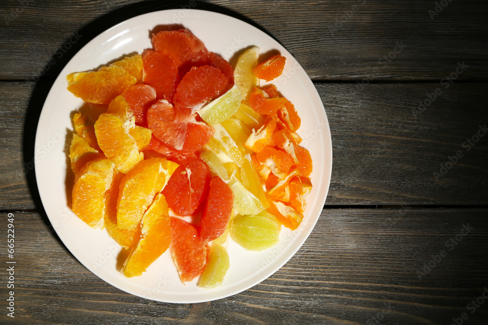 Sliced citrus fruits on plate, on wooden background Sliced citrus fruits on plate, on wooden background