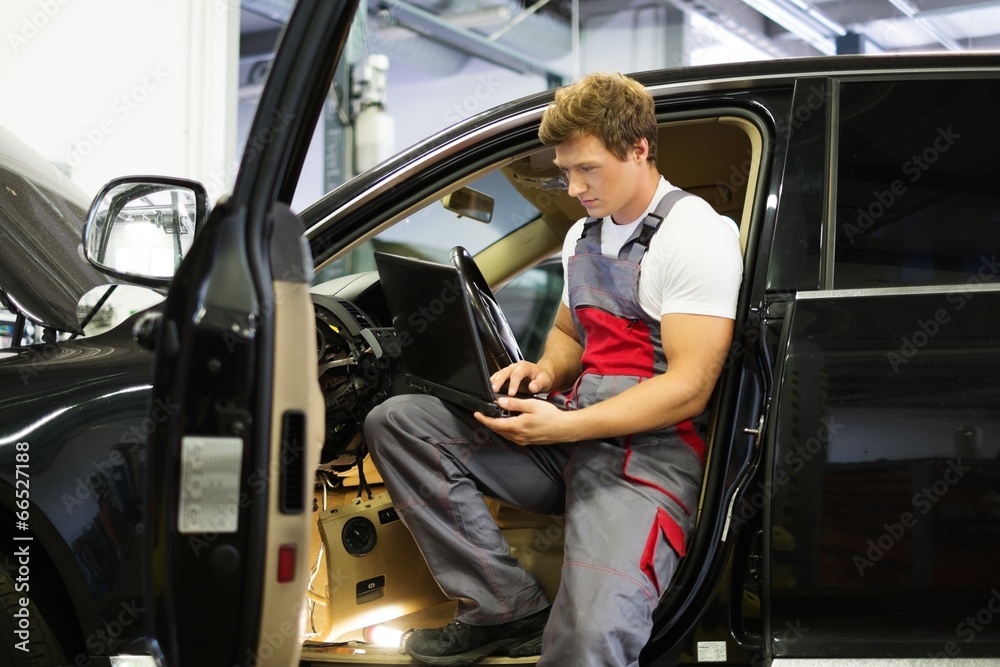 Serviceman making car diagnostics with laptop in a workshop