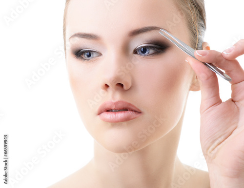 Beautiful girl plucking eyebrows with tweezers over white