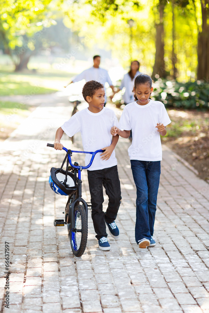 kids walking with a bike with parents behind kids walking with a bike with parents behind