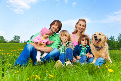 Smiling family sitting on green grass with dog